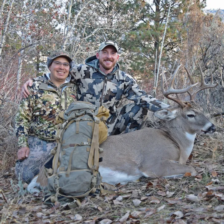 Hunters posing with deer in forest.