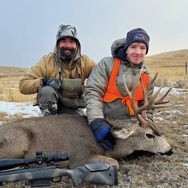 Hunters posing with a deer on grassland.