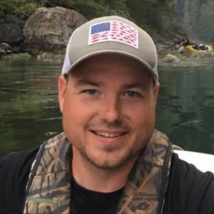Man smiling wearing cap by a river.