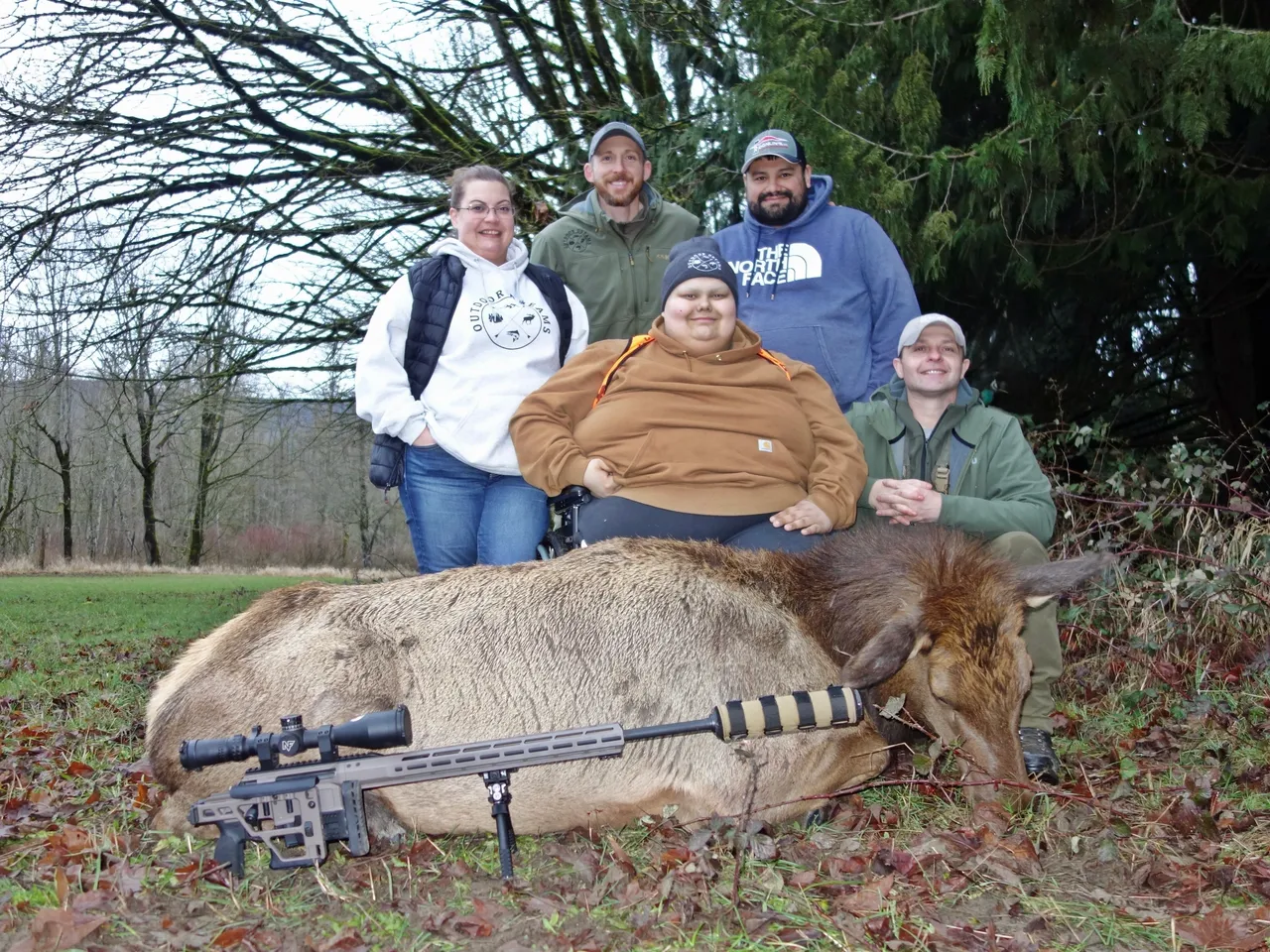 Group posing with elk in forest clearing.