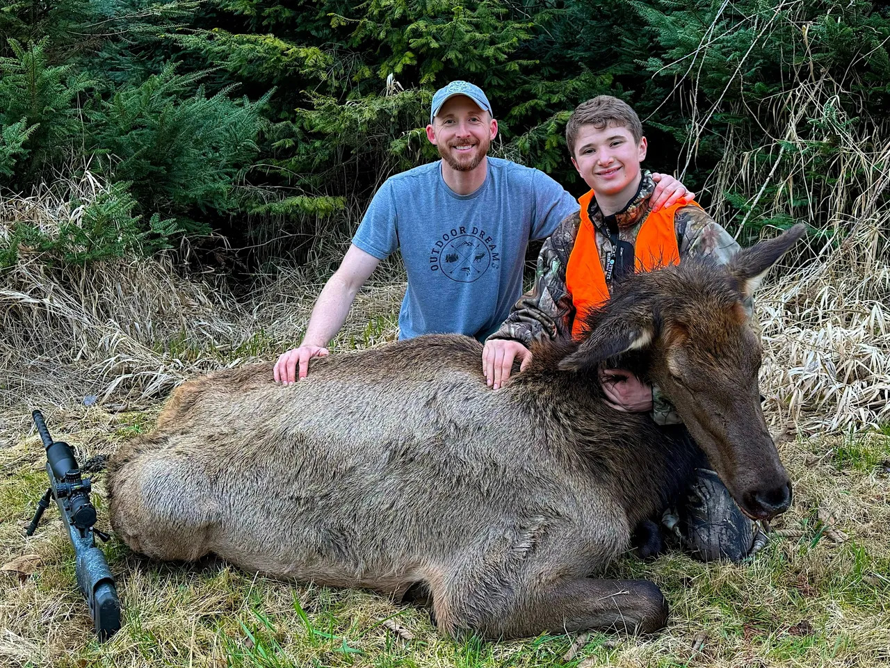 Two people with a hunted elk outdoors.