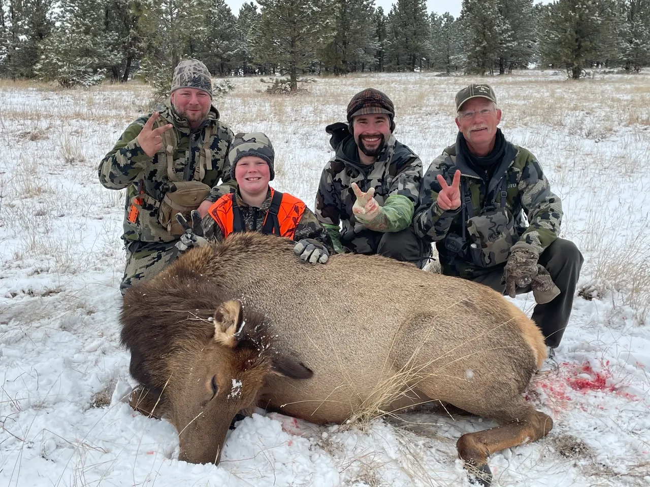 Hunters posing with elk in snowy field.