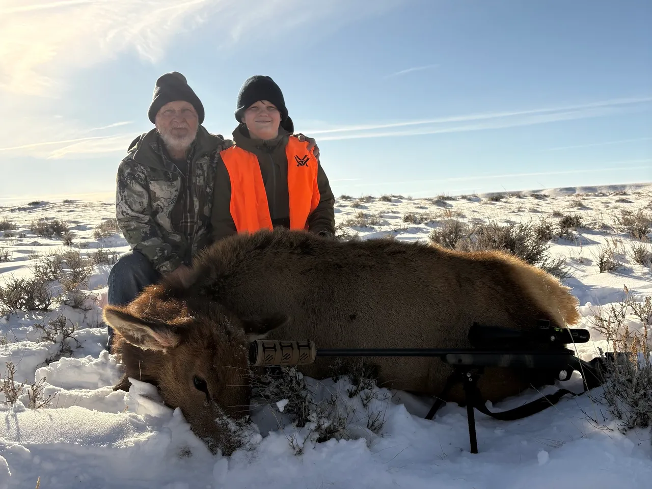 Two hunters with elk on snowy ground.