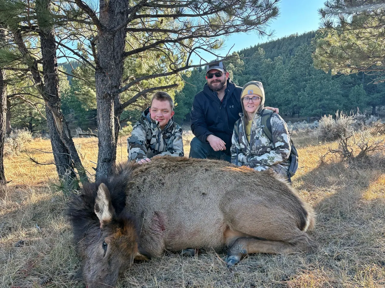 Three people posing with a hunted elk.
