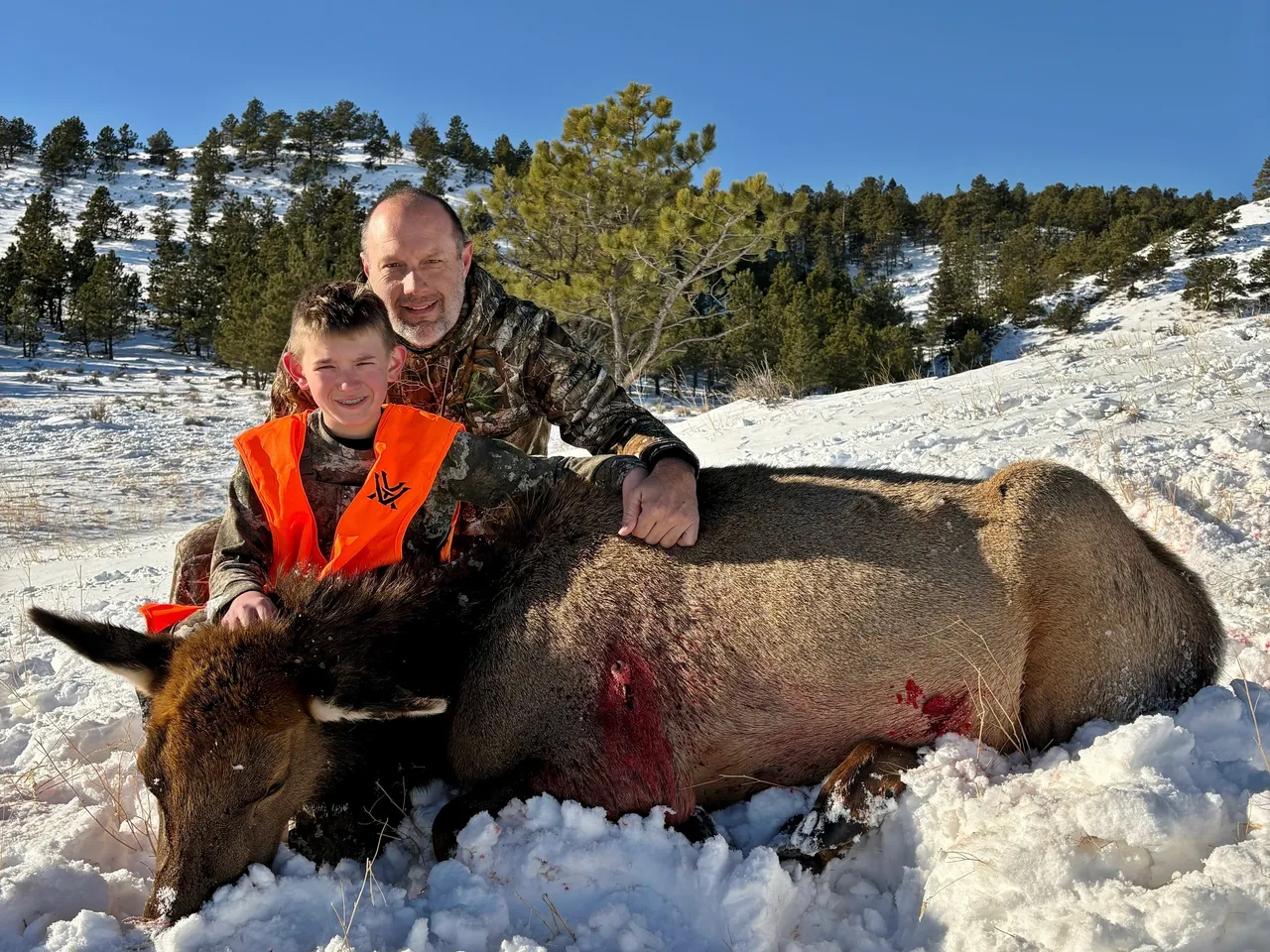 Father and son with hunted elk in snow.