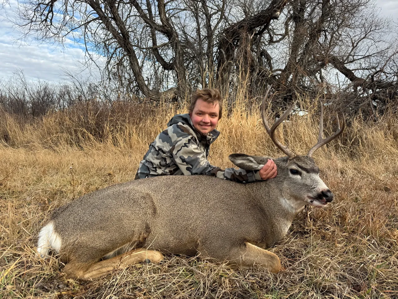Person posing with a deer in grass.