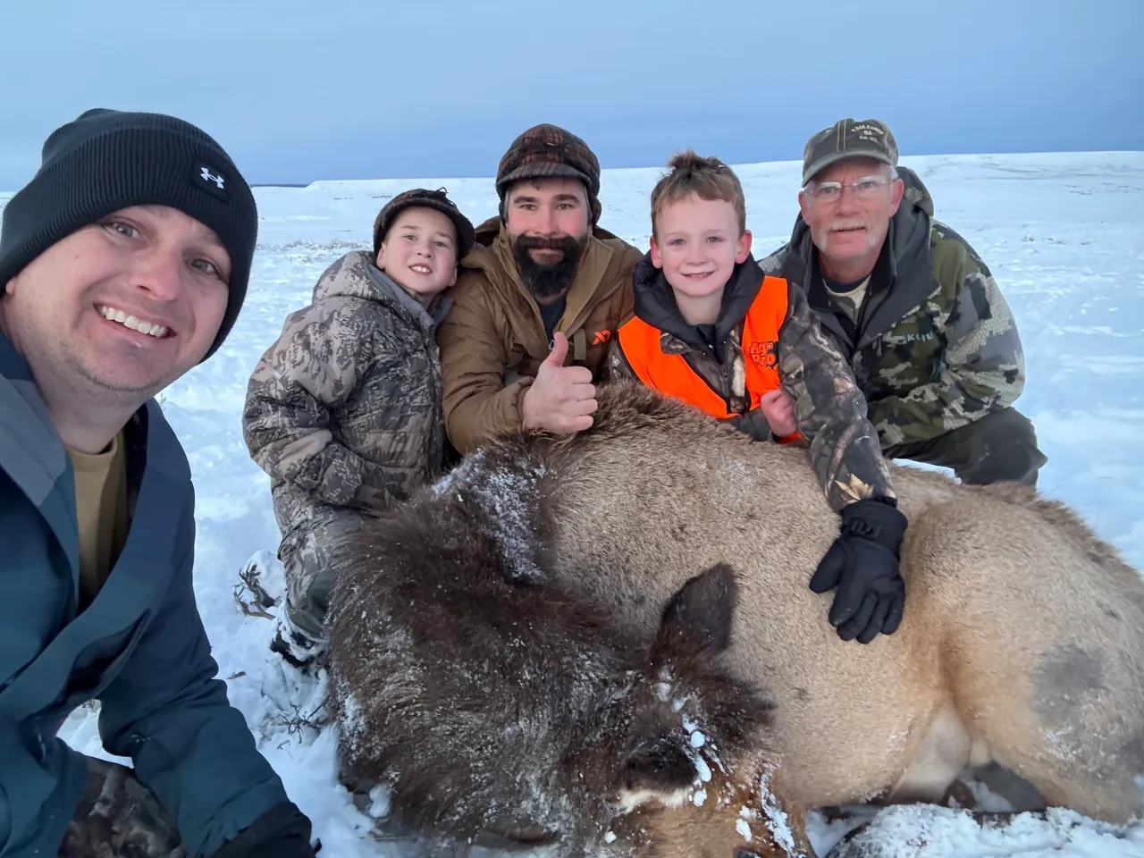 Group posing with hunted animal in snow.