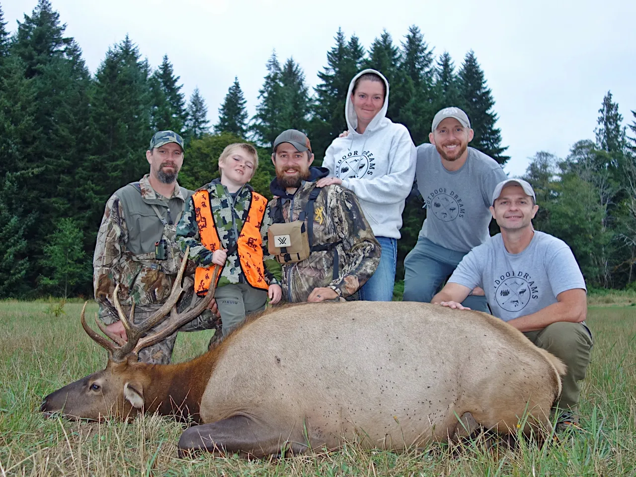 Group posing with elk in forest clearing.