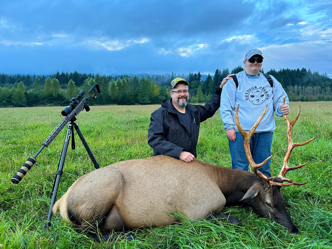 Two people pose with an elk outdoors.