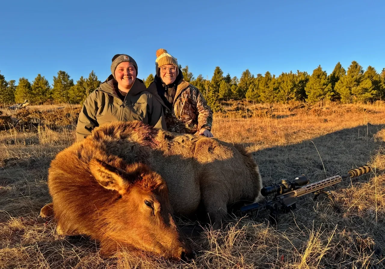 Hunters posing with elk in field.