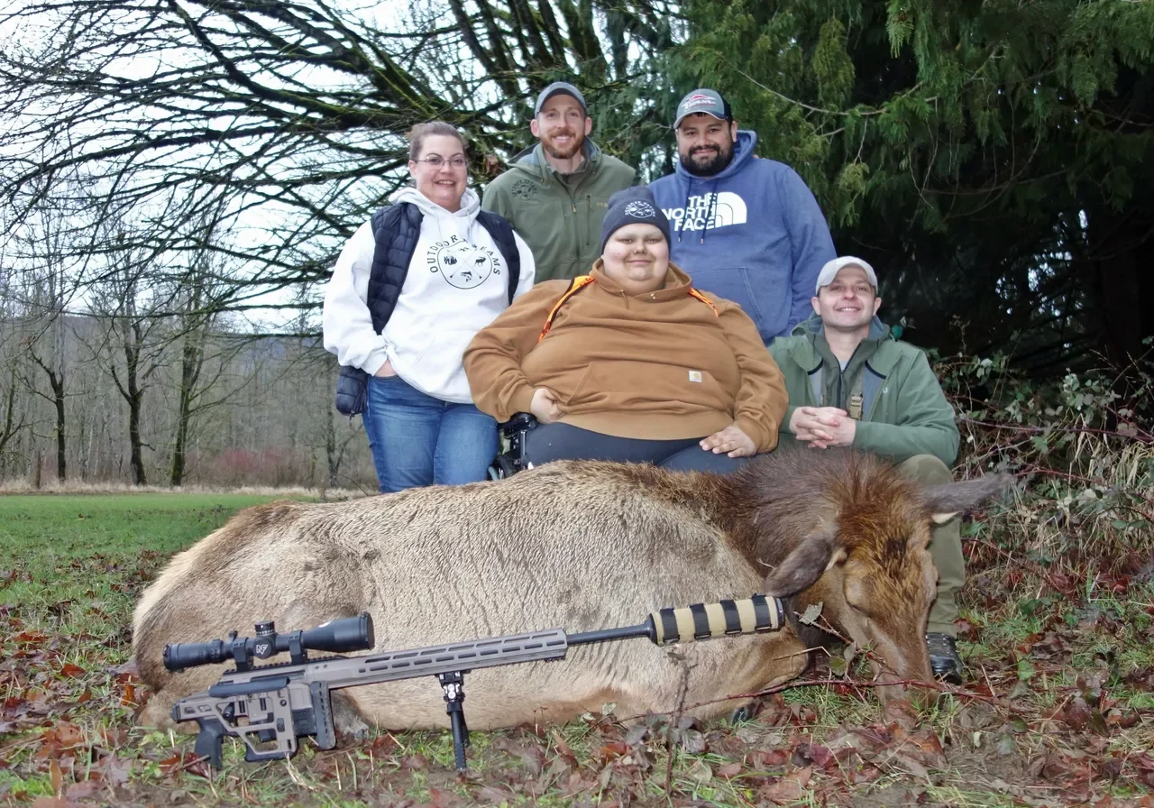 Group posing with elk in forest clearing.