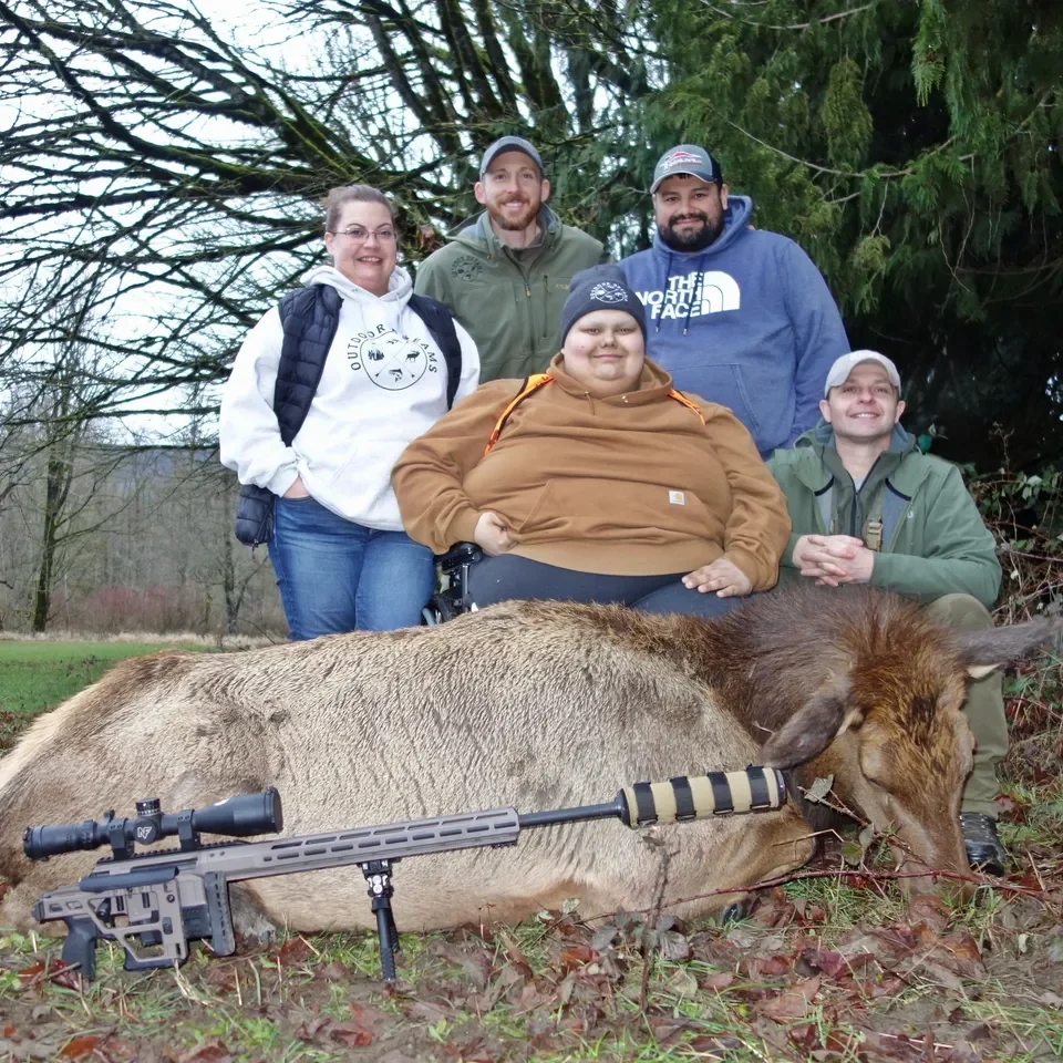 Group posing with elk in forest clearing.