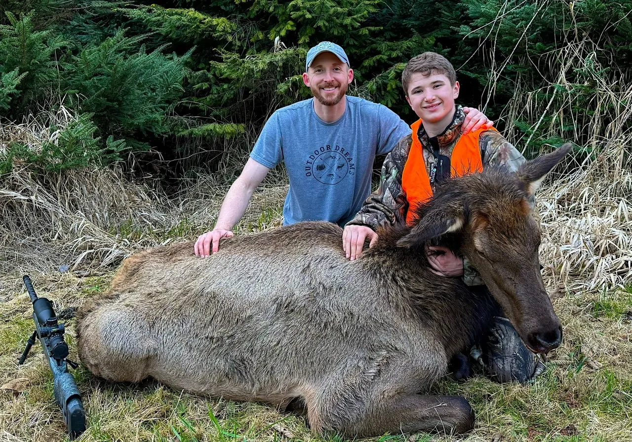 Two people with a hunted elk outdoors.