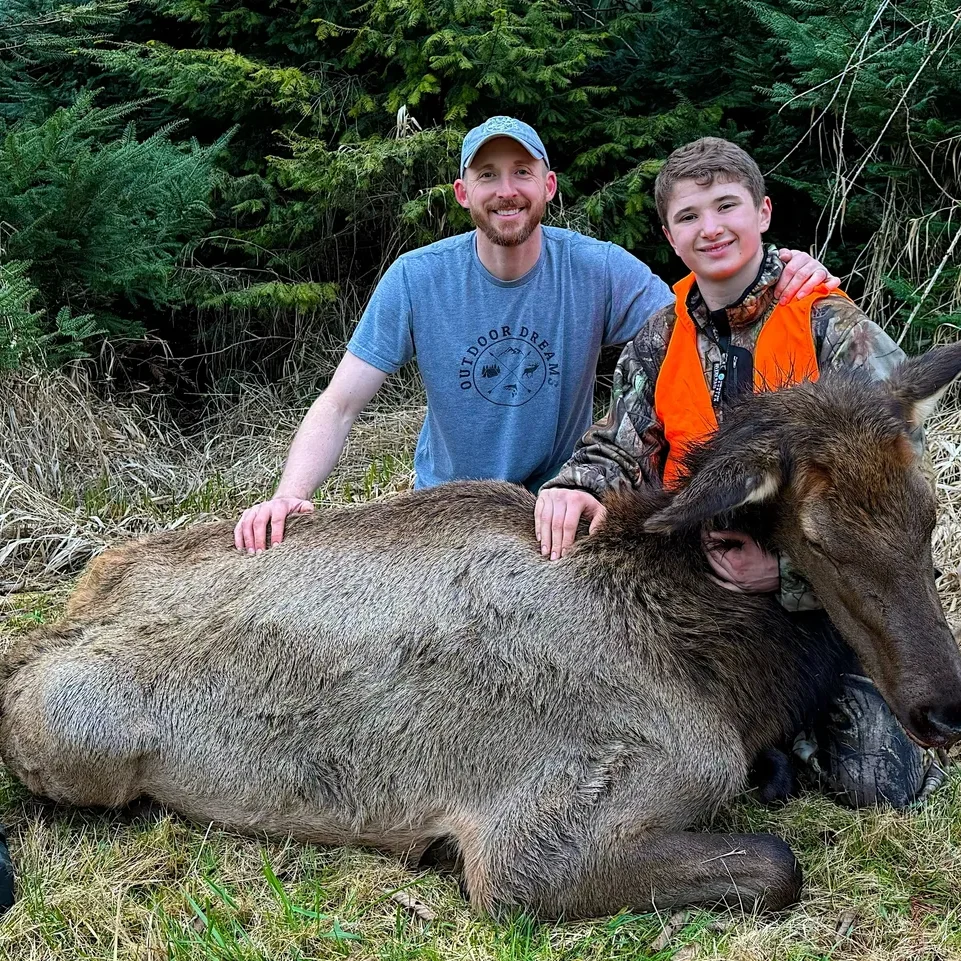 Two people with a hunted elk outdoors.