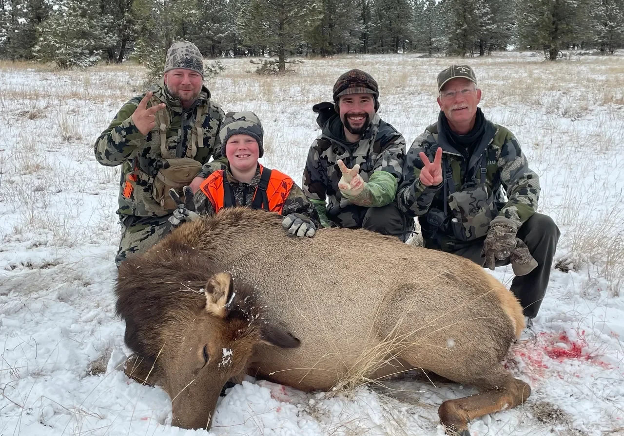 Hunters posing with elk in snowy field.