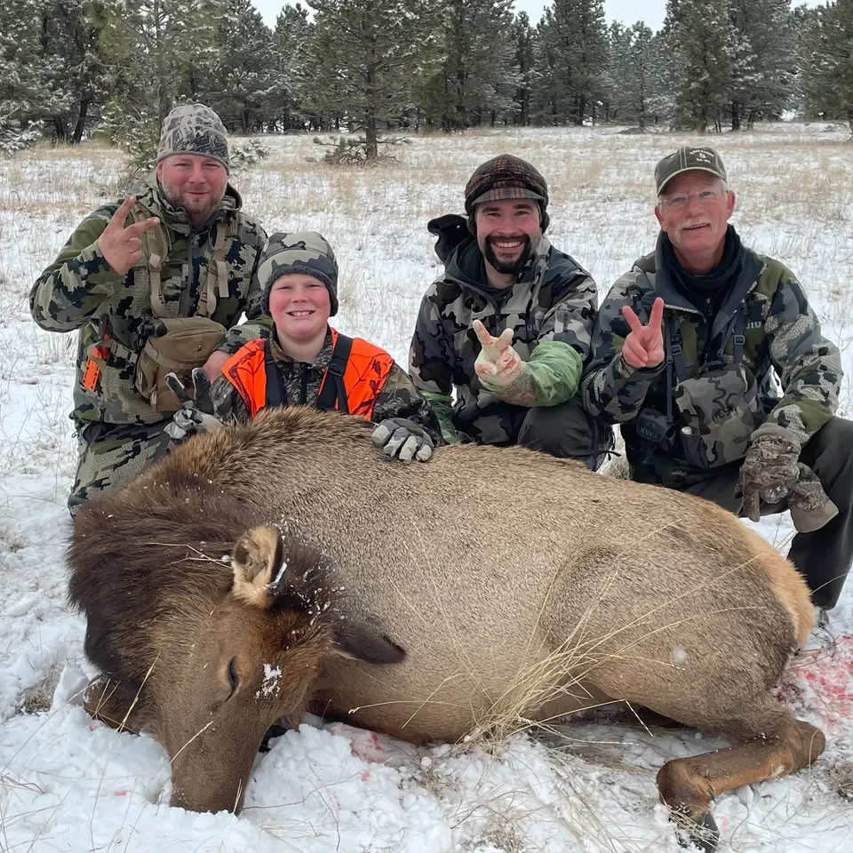 Hunters posing with elk in snowy field.