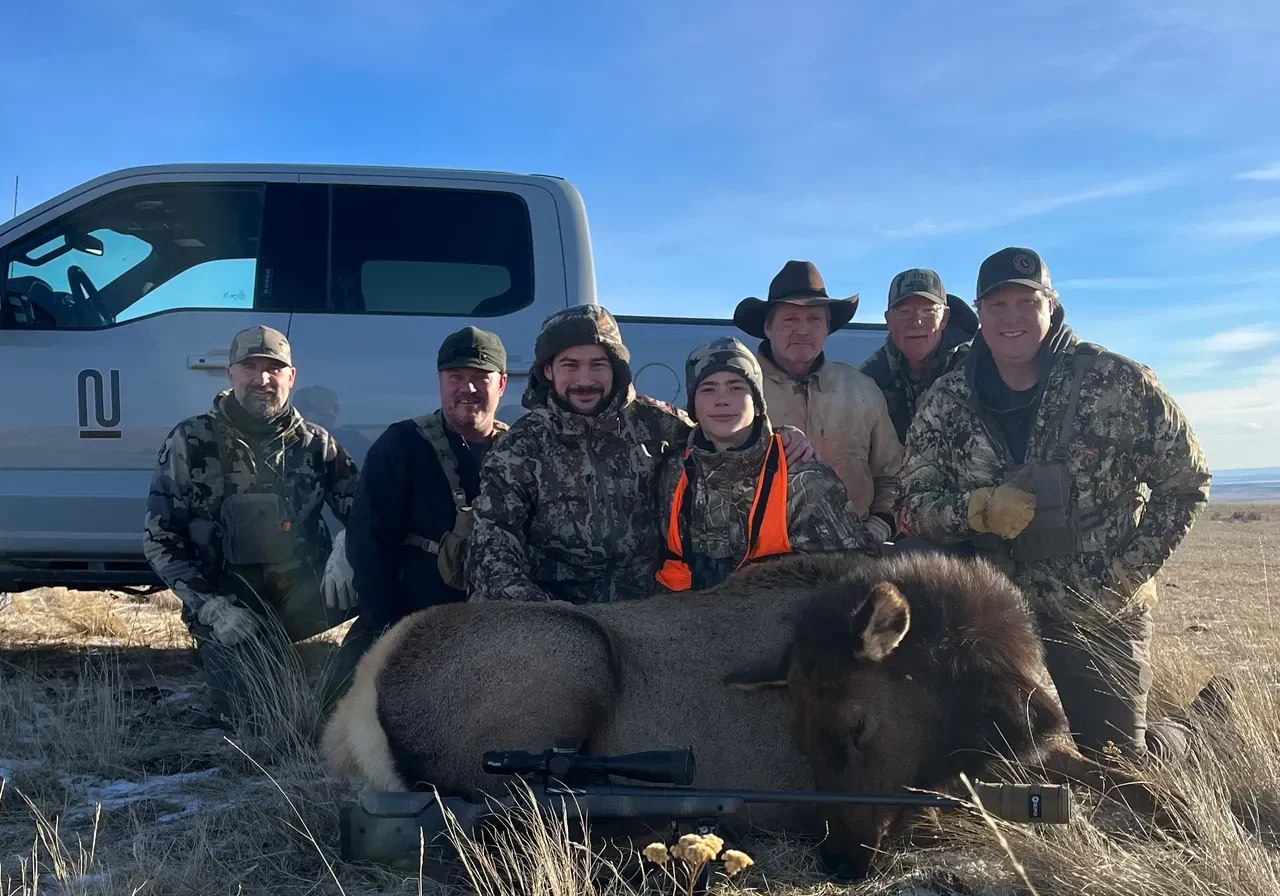 Hunters posing with bison in field.
