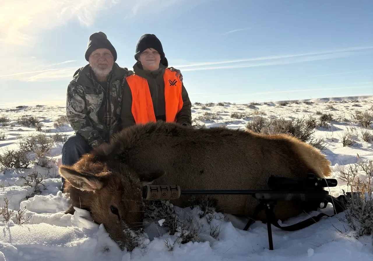 Two hunters with elk on snowy ground.