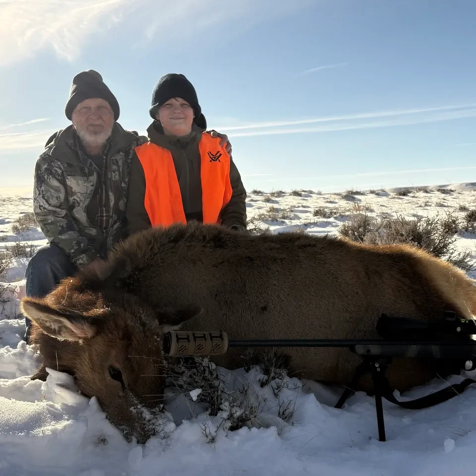 Two hunters with elk on snowy ground.