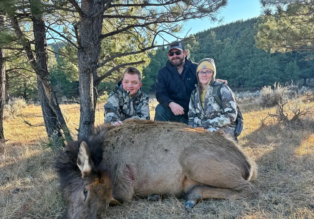 Three people posing with a hunted elk.
