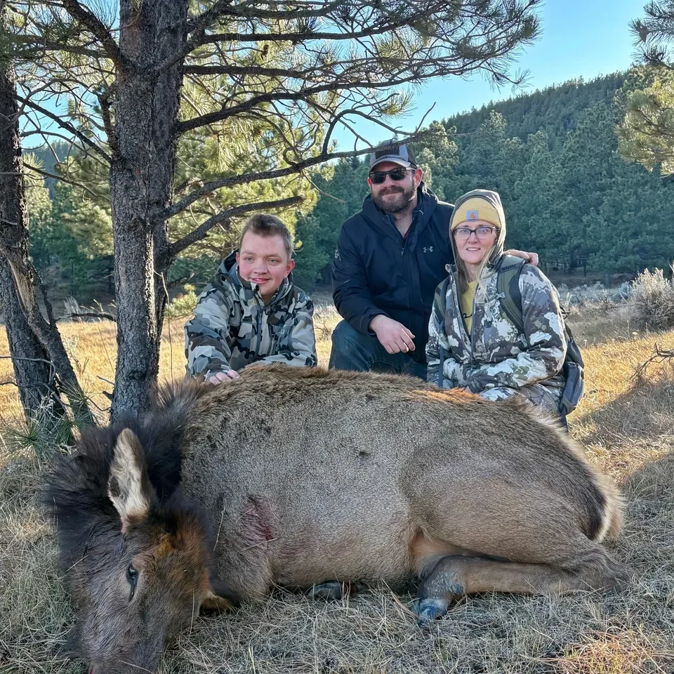 Three people posing with a hunted elk.