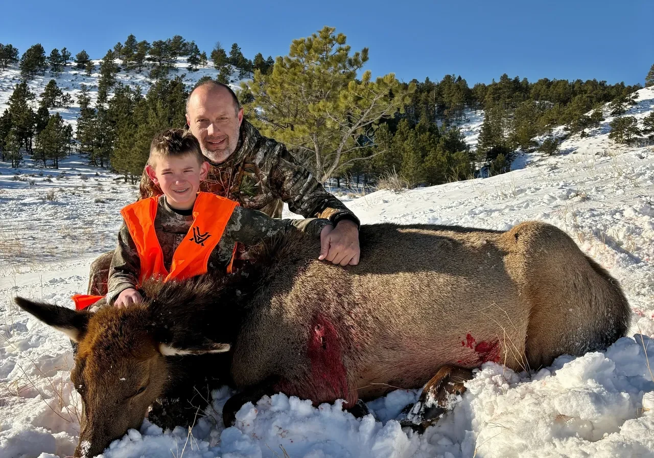 Father and son with hunted elk in snow.
