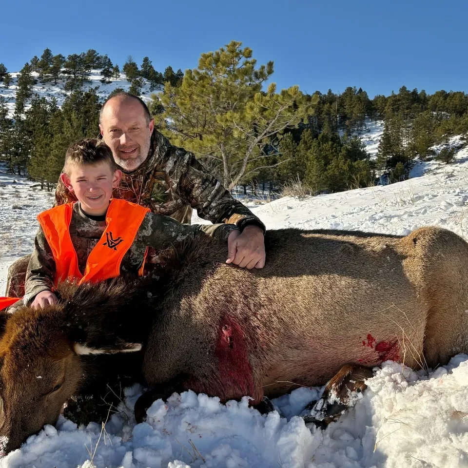 Father and son with hunted elk in snow.