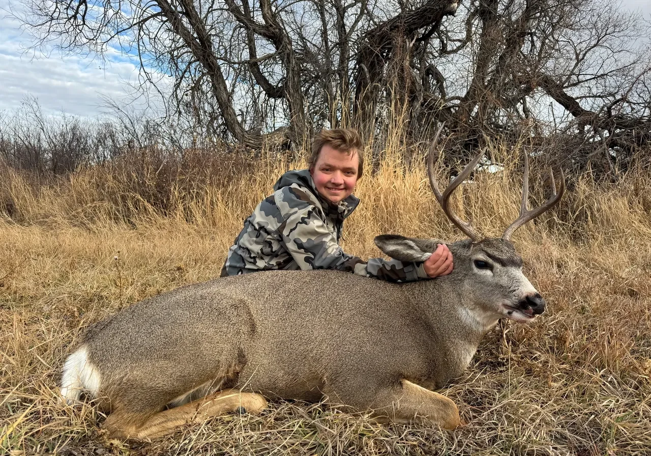 Person posing with a deer in grass.