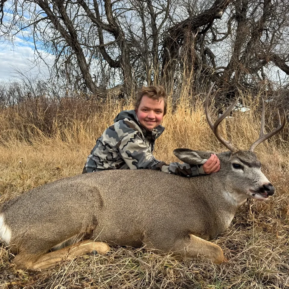 Person posing with a deer in grass.