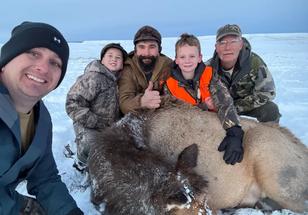 Group posing with hunted animal in snow.