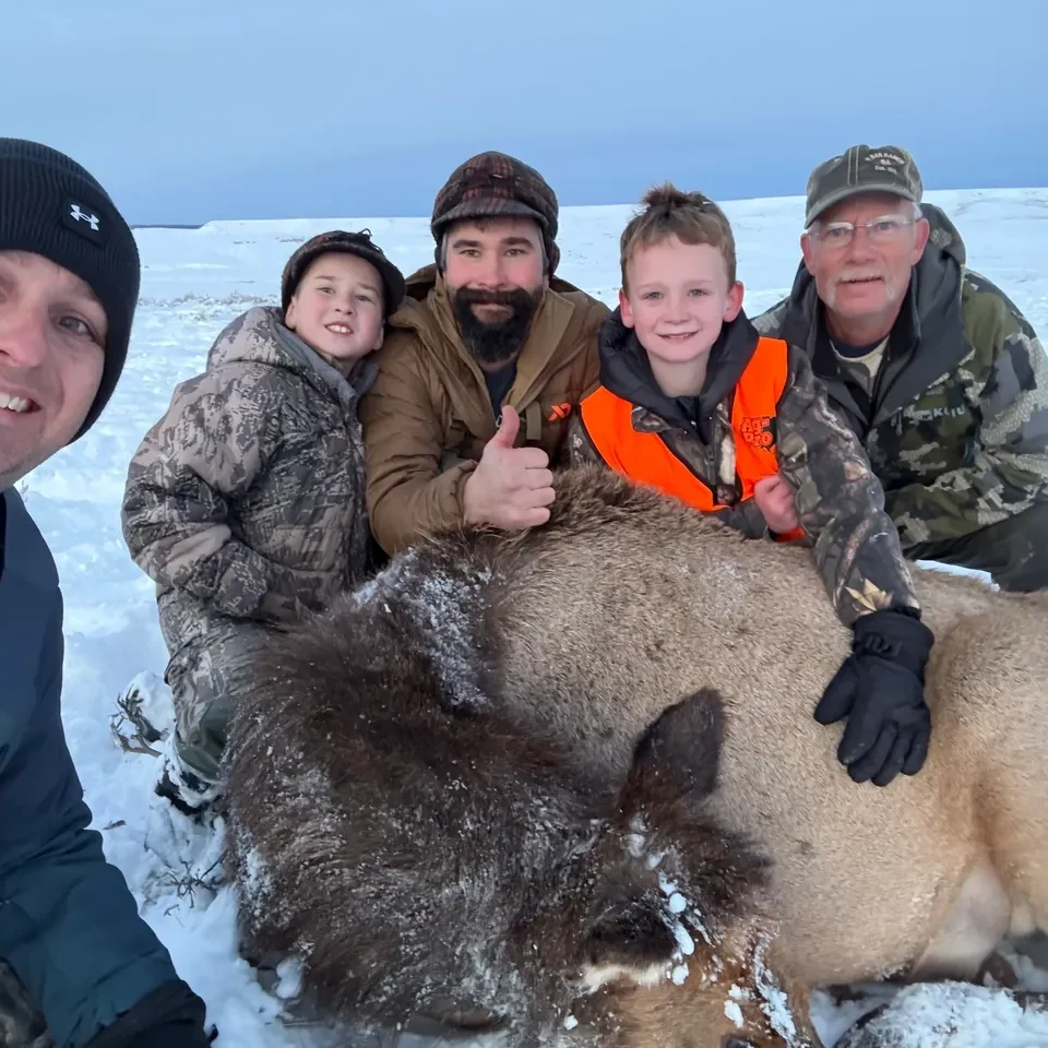 Group posing with hunted animal in snow.