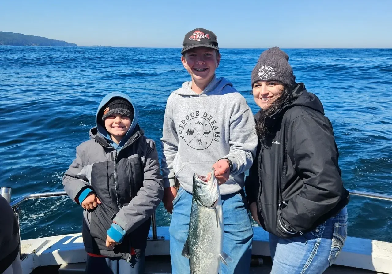 Three people on boat holding a fish.