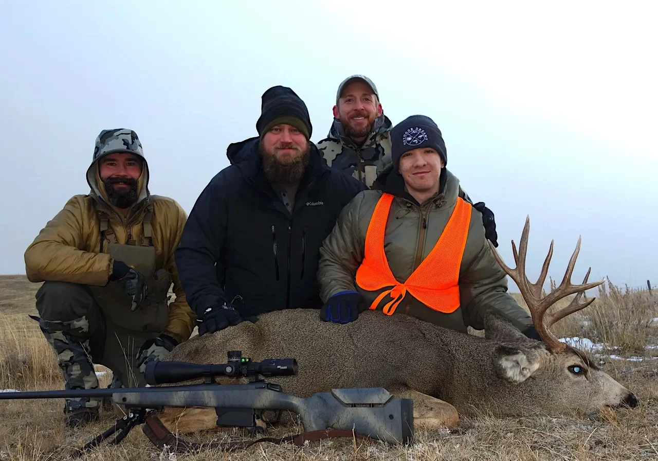 Four hunters posing with a deer trophy.