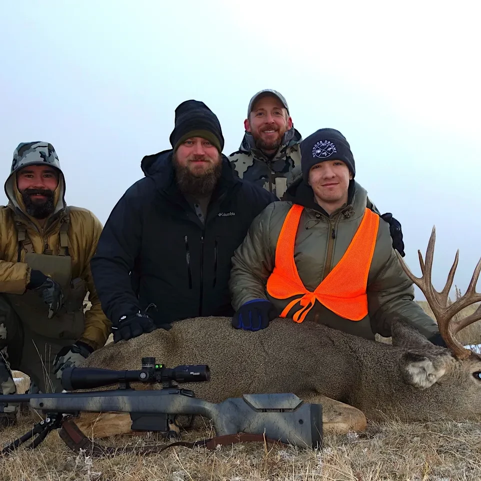 Four hunters posing with a deer trophy.