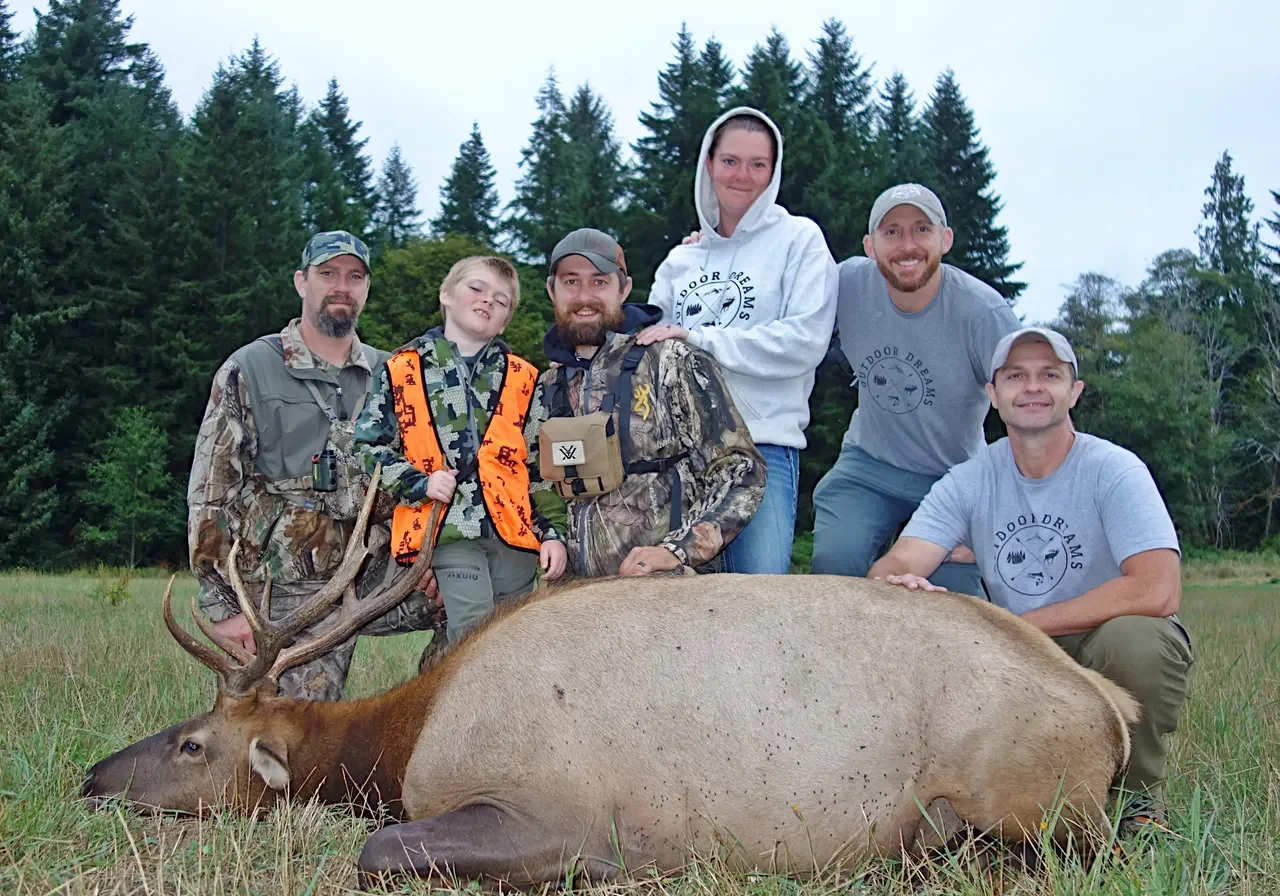 Group posing with elk in forest clearing.