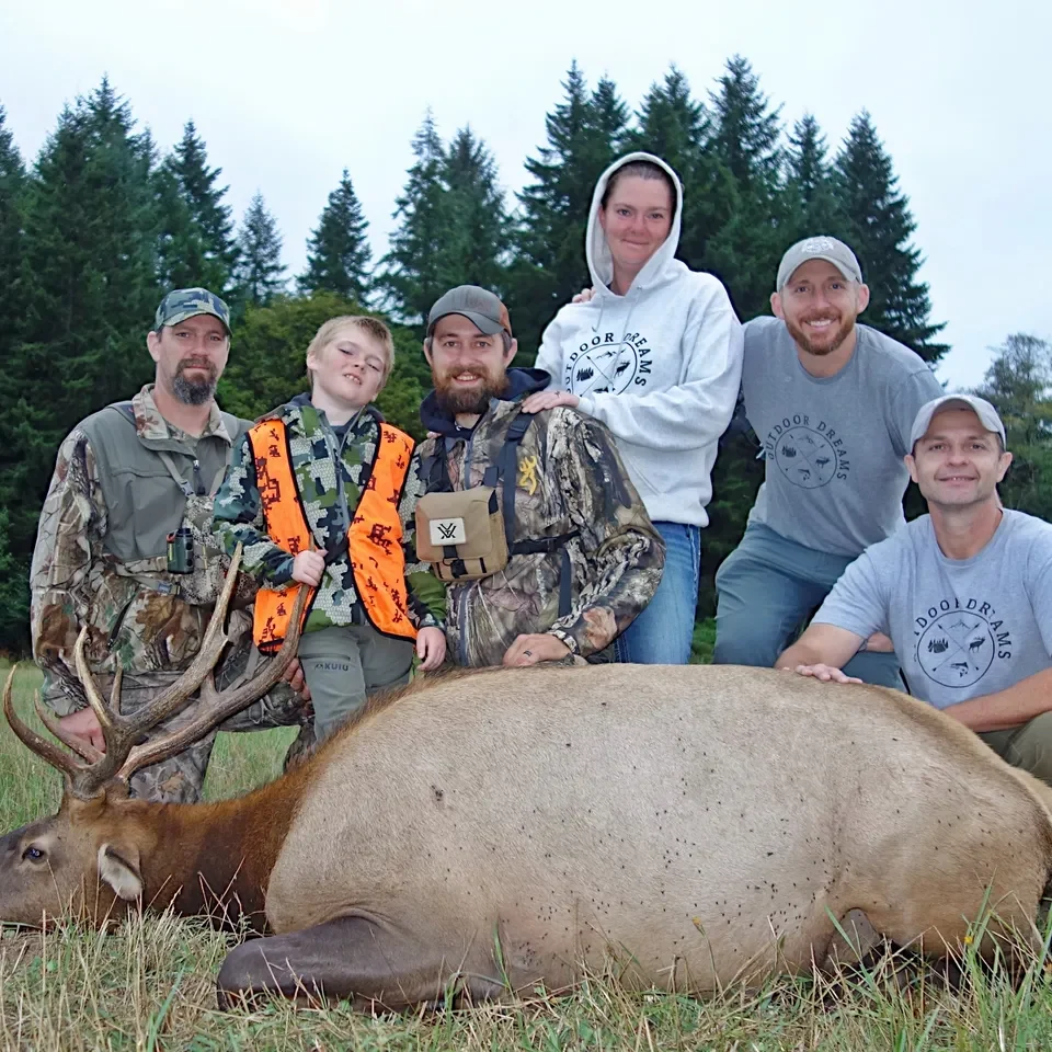 Group posing with elk in forest clearing.